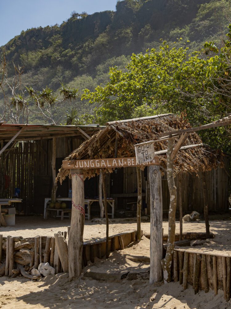 Rustic sign marking the entrance to Nunggalan Beach on Bali's southern coast, surrounded by lush jungle and cliffs.