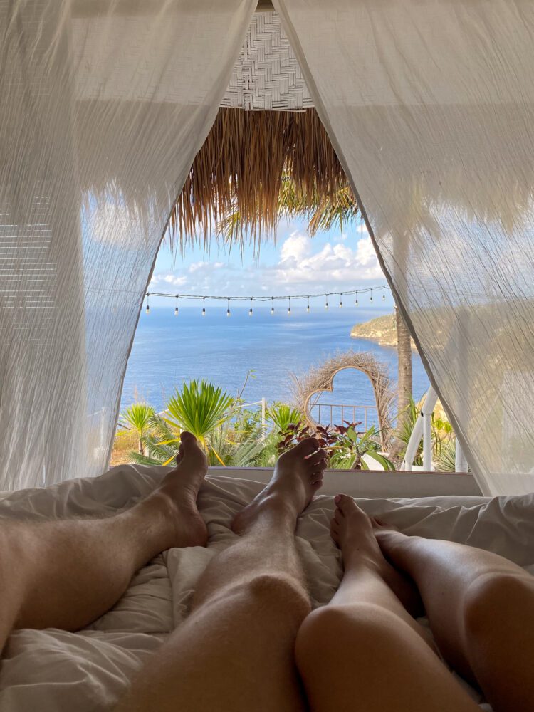 Relaxing oceanfront view from a breezy cliffside bungalow in Nusa Penida, framed by flowing curtains and tropical greenery.