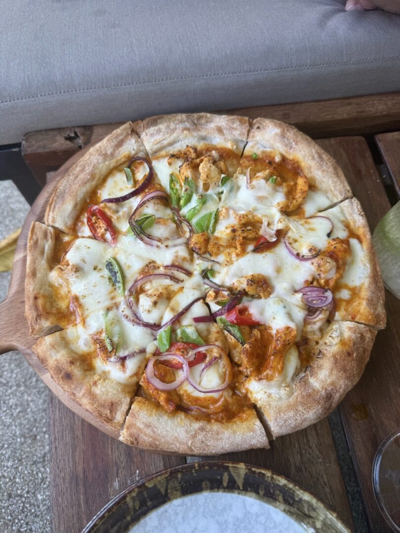 Panang curry pizza served poolside at Rayavadee Resort, topped with melted cheese, red onions, bell peppers, and Thai-spiced chicken for a flavorful fusion twist.
