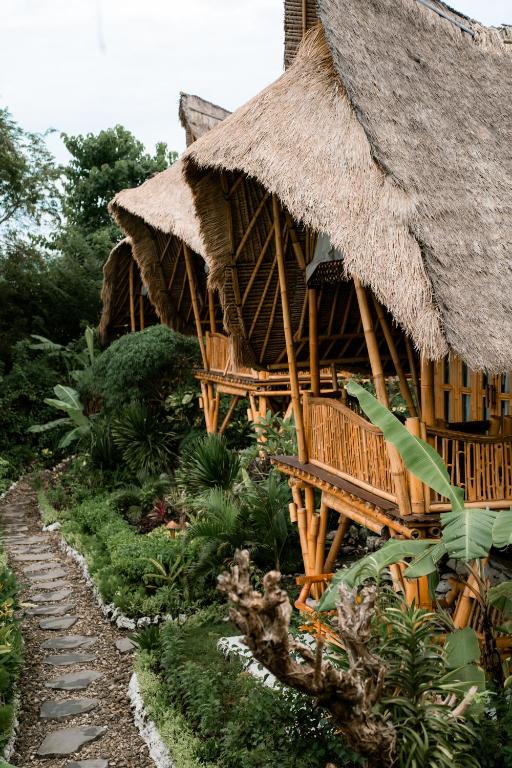Stone path leading past bamboo villas with thatched roofs nestled in tropical jungle at Bambu Green Suites.