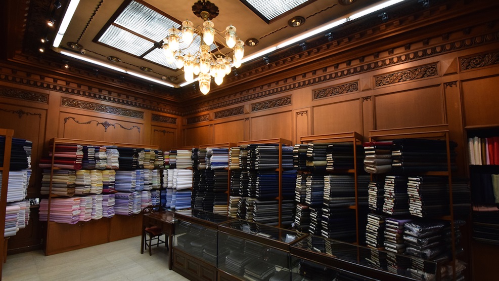 Wall-to-wall fabric bolts line the shelves at Peninsula Tailors in Bangkok, an elegant custom tailoring shop known for its classic wood-paneled interior and personalized service.