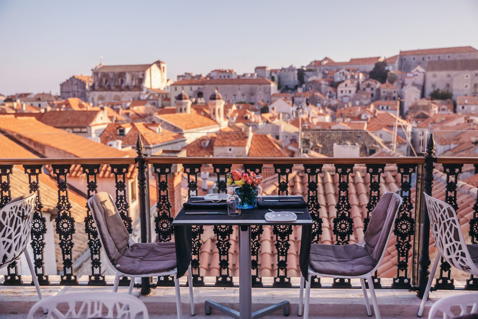 Romantic rooftop dining setup at Prijeko Palace in Dubrovnik, with a flower-topped table overlooking the terracotta rooftops and historic skyline of the Old Town at golden hour.