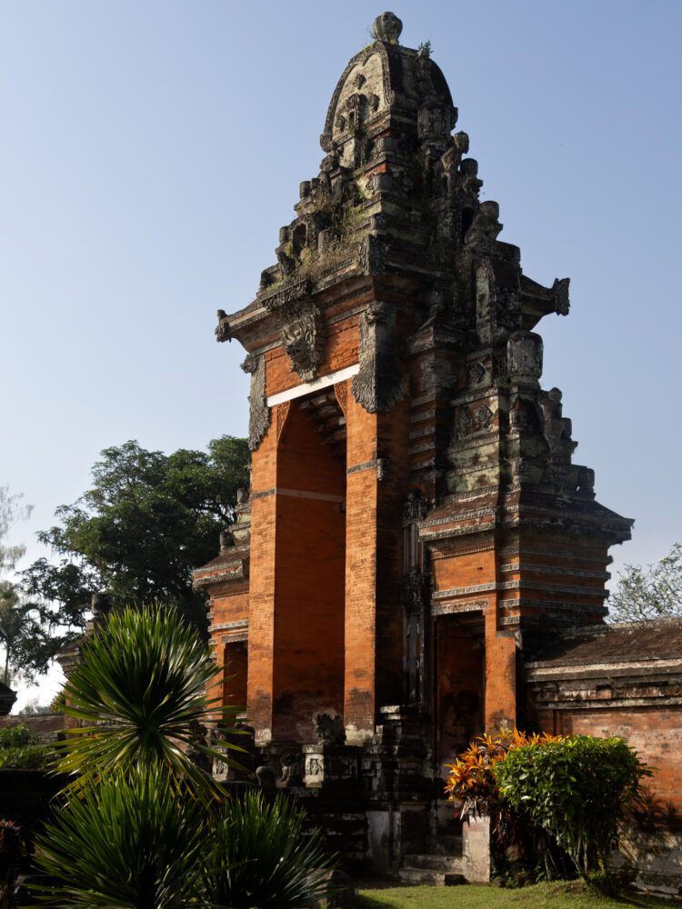 Ornate red-brick entrance of Pura Taman Ayun temple in Bali, showcasing traditional Balinese architecture against a clear blue sky.