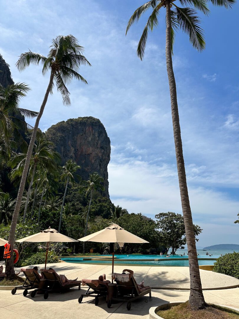 Rayavadee Resort’s beachfront infinity pool surrounded by palm trees and sun loungers, with stunning views of the limestone cliffs and turquoise waters of Railay Beach.