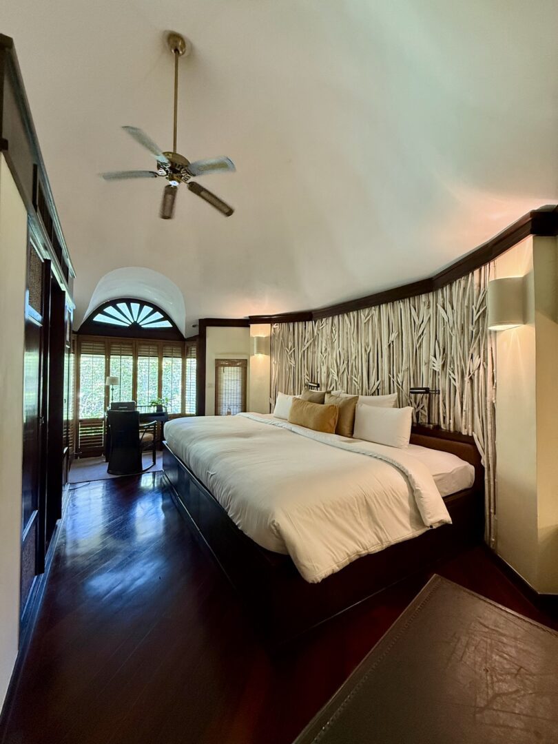 Elegant villa bedroom at Rayavadee Resort featuring a vaulted ceiling, rich wooden floors, and a plush king-size bed with nature-inspired decor and garden-facing windows.