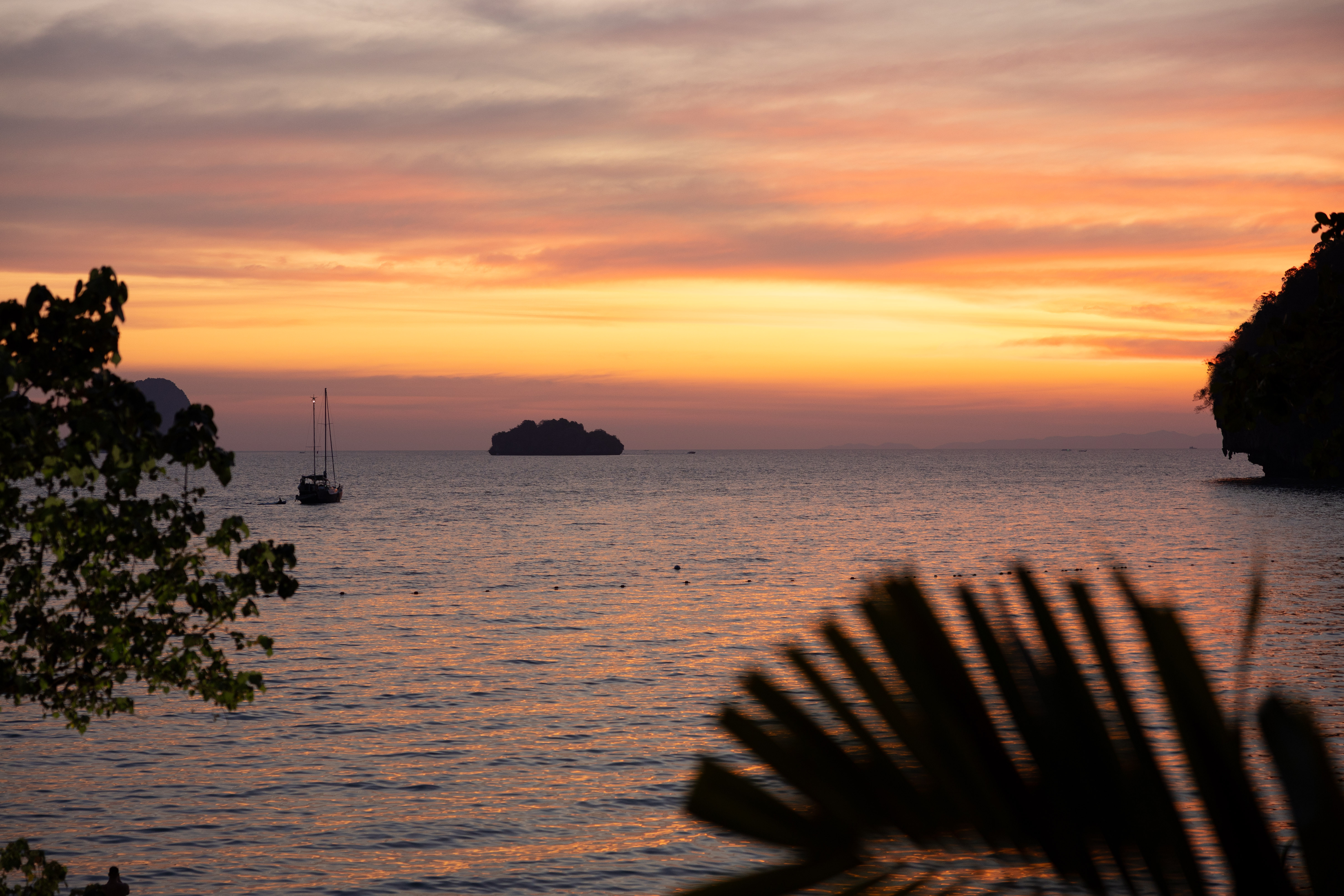 Fiery sunset over the Andaman Sea viewed from Railay Beach, with silhouetted sailboats and limestone islets completing the dreamy tropical seascape near Rayavadee Resort.