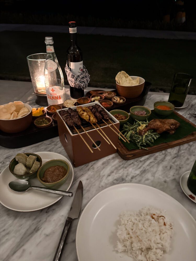 Romantic Indonesian feast served al fresco at Alila Villas Uluwatu, with skewered satay, sambals, and rice set under candlelight.