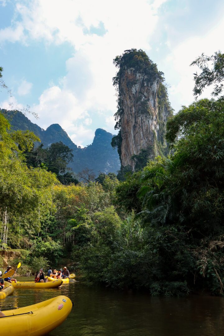 Canoers paddle along the Sok River beneath towering limestone cliffs and dense jungle foliage in Khao Sok National Park, Thailand.