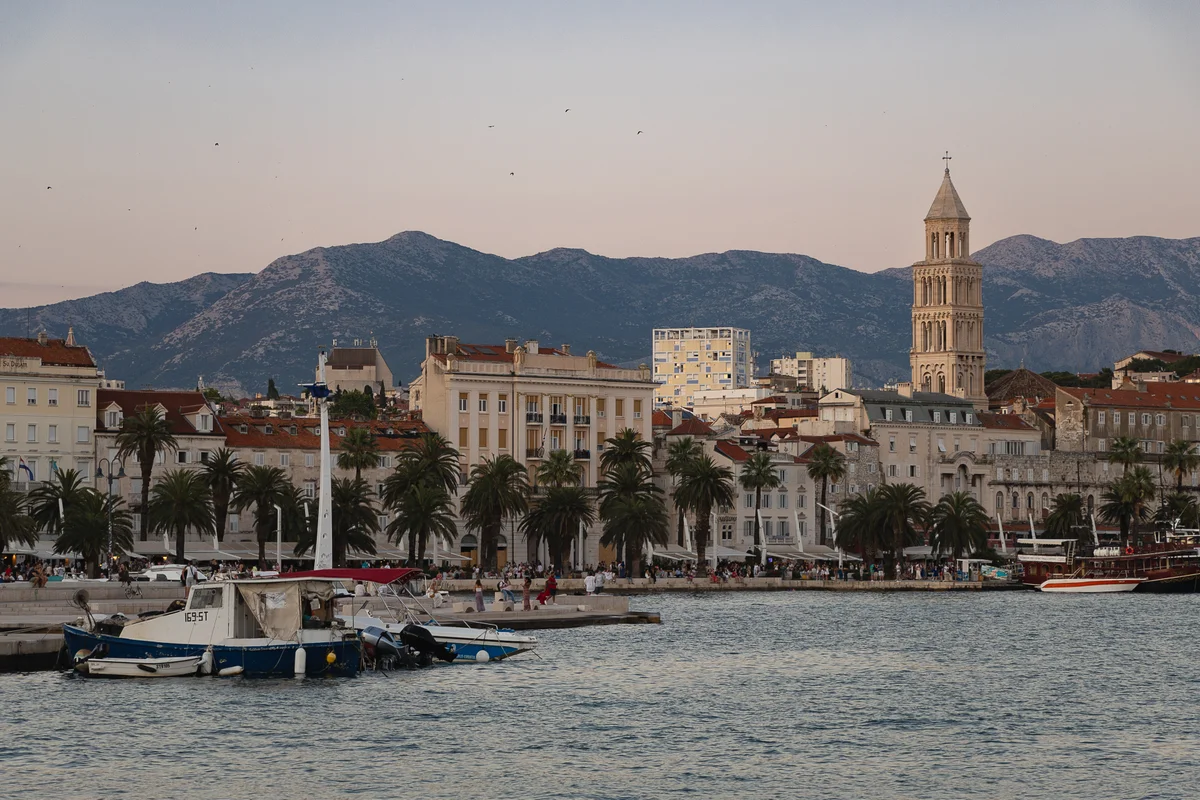 Split Croatia's waterfront promenade at golden hour, with boats docked along the harbor and the bell tower of Saint Domnius rising against the mountain backdrop.
