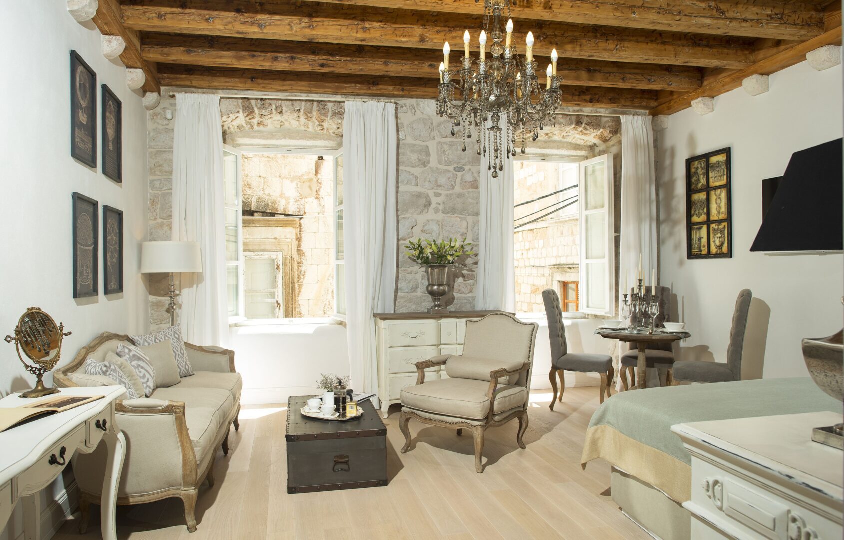 Elegant suite at St. Joseph’s Boutique Hotel in Dubrovnik featuring exposed stone walls, vintage furnishings, and a grand chandelier, with open windows looking out onto the Old Town’s historic charm.