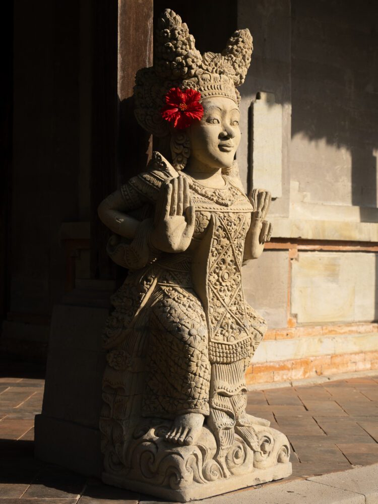Intricate stone statue adorned with a red hibiscus flower at Taman Ayun Temple in Bali.