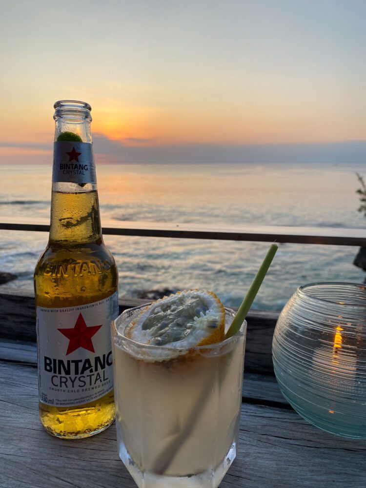 Sunset ocean view with a bottle of Bintang Crystal beer and a passionfruit cocktail at Rock Bar in Uluwatu.