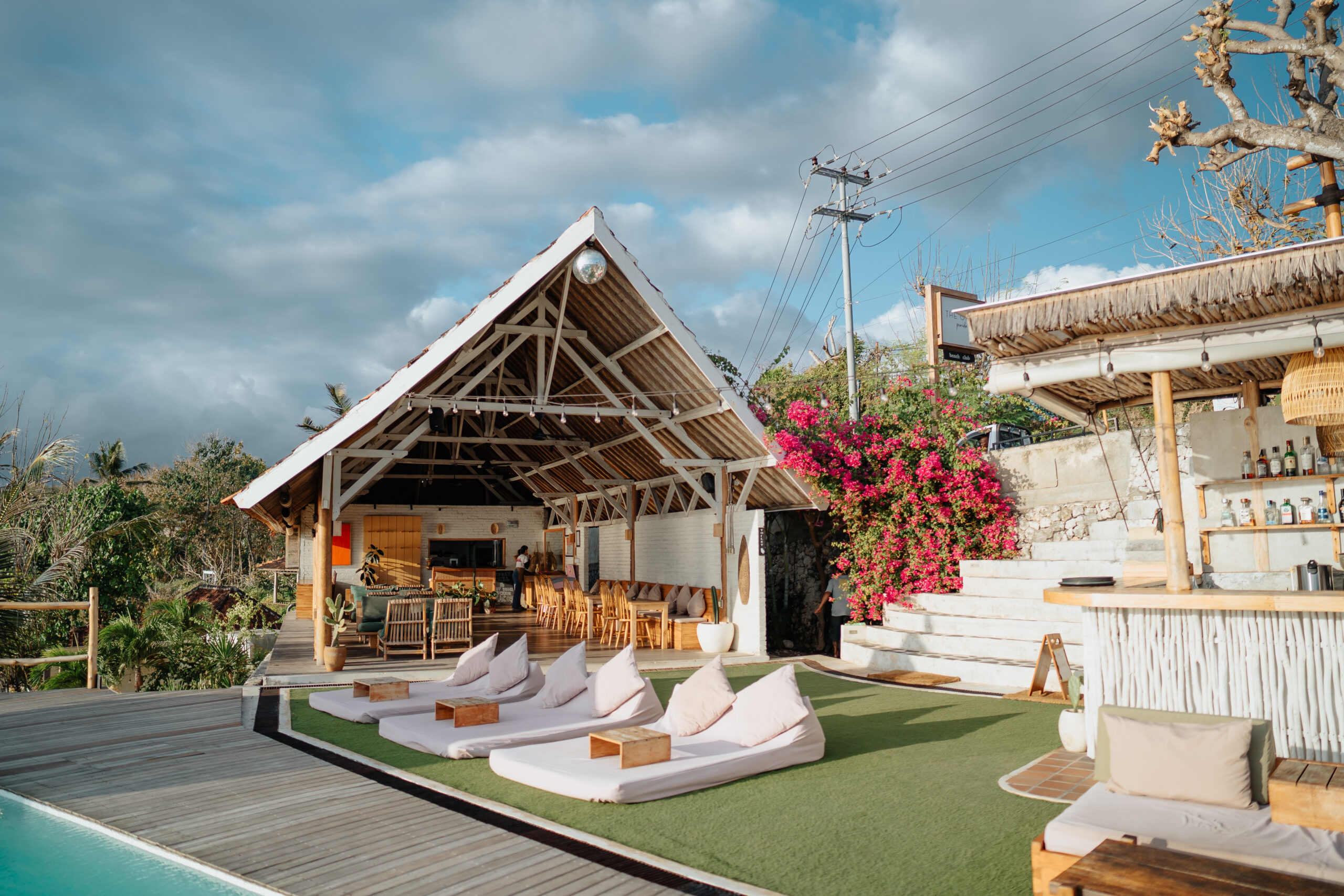 Relaxed open-air setting at The Chill Penida, featuring poolside lounge beds, a bamboo bar, and tropical flowers—all framed by rustic island charm and sweeping views in Nusa Penida.