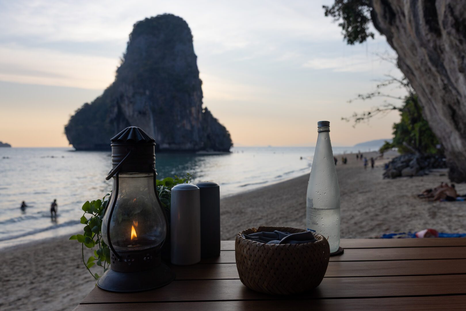 Romantic beachfront table at The Grotto, Rayavadee Resort, set against the dramatic backdrop of limestone cliffs and a serene Andaman Sea sunset.