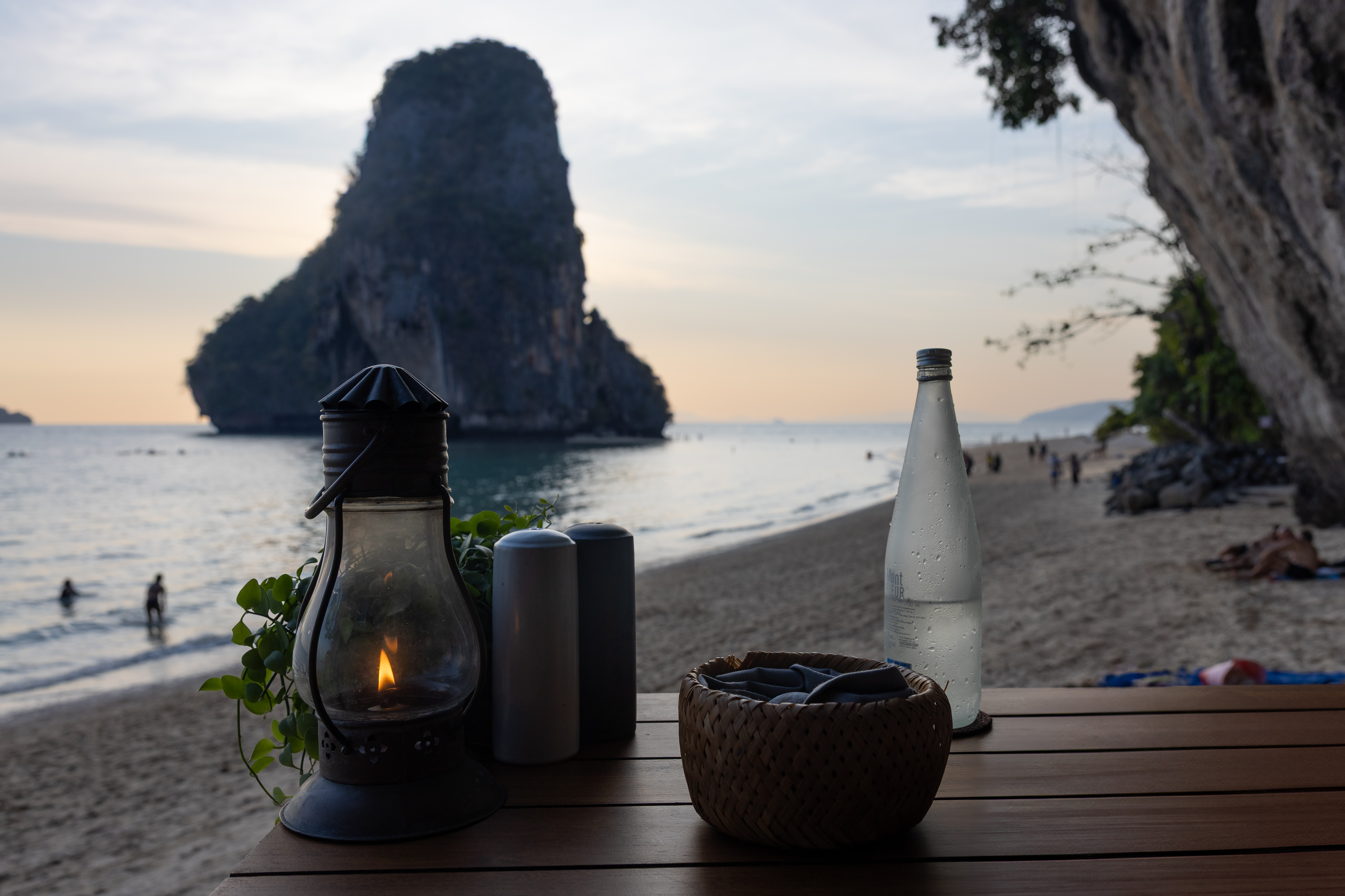 Romantic beachfront table at The Grotto, Rayavadee Resort, set against the dramatic backdrop of limestone cliffs and a serene Andaman Sea sunset.