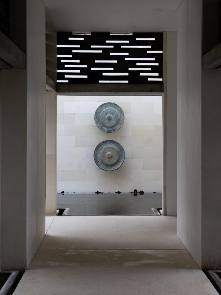 Minimalist corridor with traditional Balinese gongs at Alila Villas Uluwatu, blending contemporary design and local artistry.