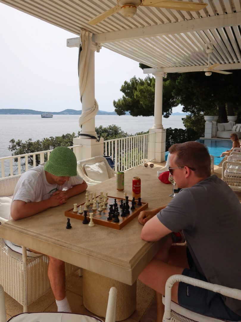 Two men playing chess on a shaded terrace at a luxury villa in Dubrovnik, overlooking the sea.
