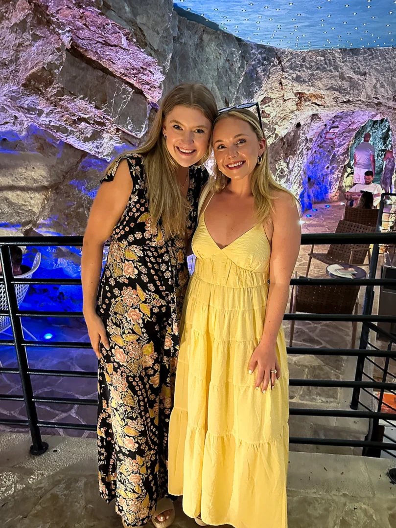 Two women smiling together inside Dubrovnik’s Cave Bar More, surrounded by colorful lights and natural rock walls in a unique underground setting.