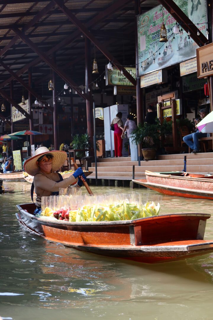 A local vendor in a wide-brimmed hat paddles a wooden boat filled with fresh fruit at Damnoen Saduak Floating Market, one of Thailand’s most iconic floating bazaars.