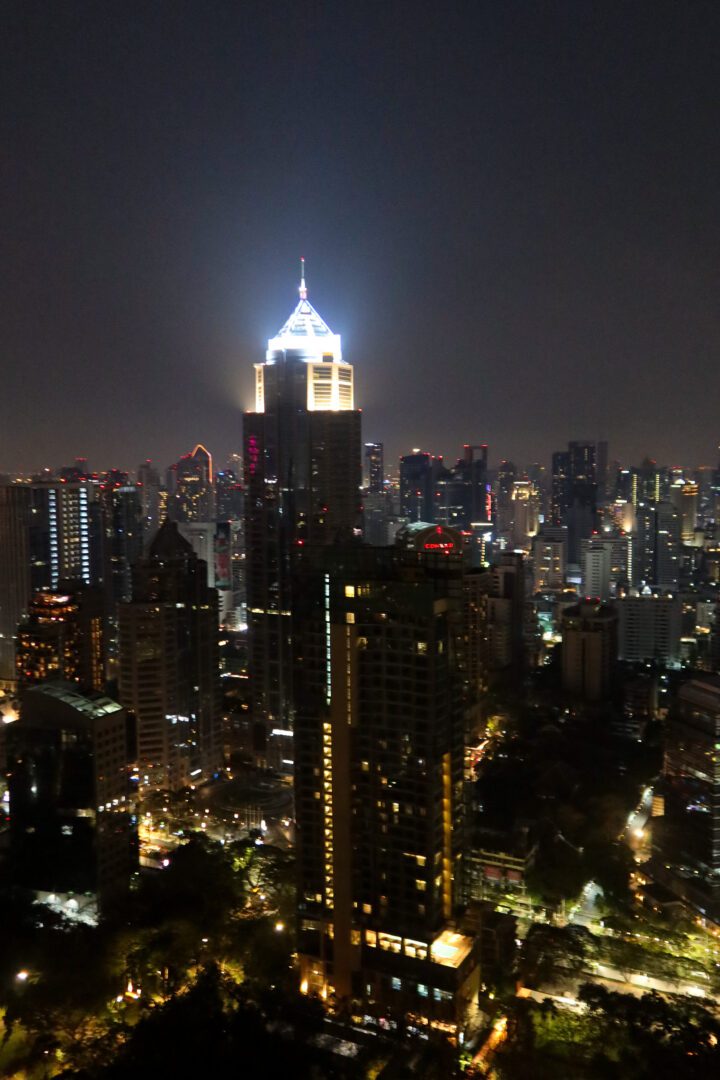 The Bangkok skyline glows with towering skyscrapers and city lights, as seen from the rooftop of Kimpton Maa-Lai during a clear night.
