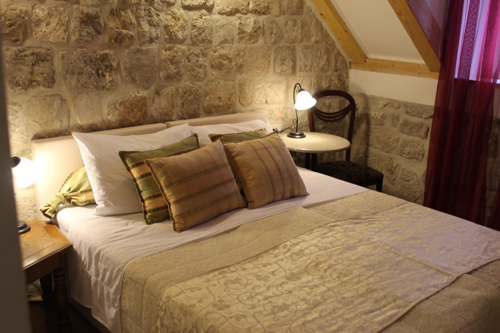 Intimate stone-walled guest room at Villa Sigurata in Dubrovnik’s Old Town, with soft lighting, rustic charm, and a plush bed layered in golden-toned pillows.