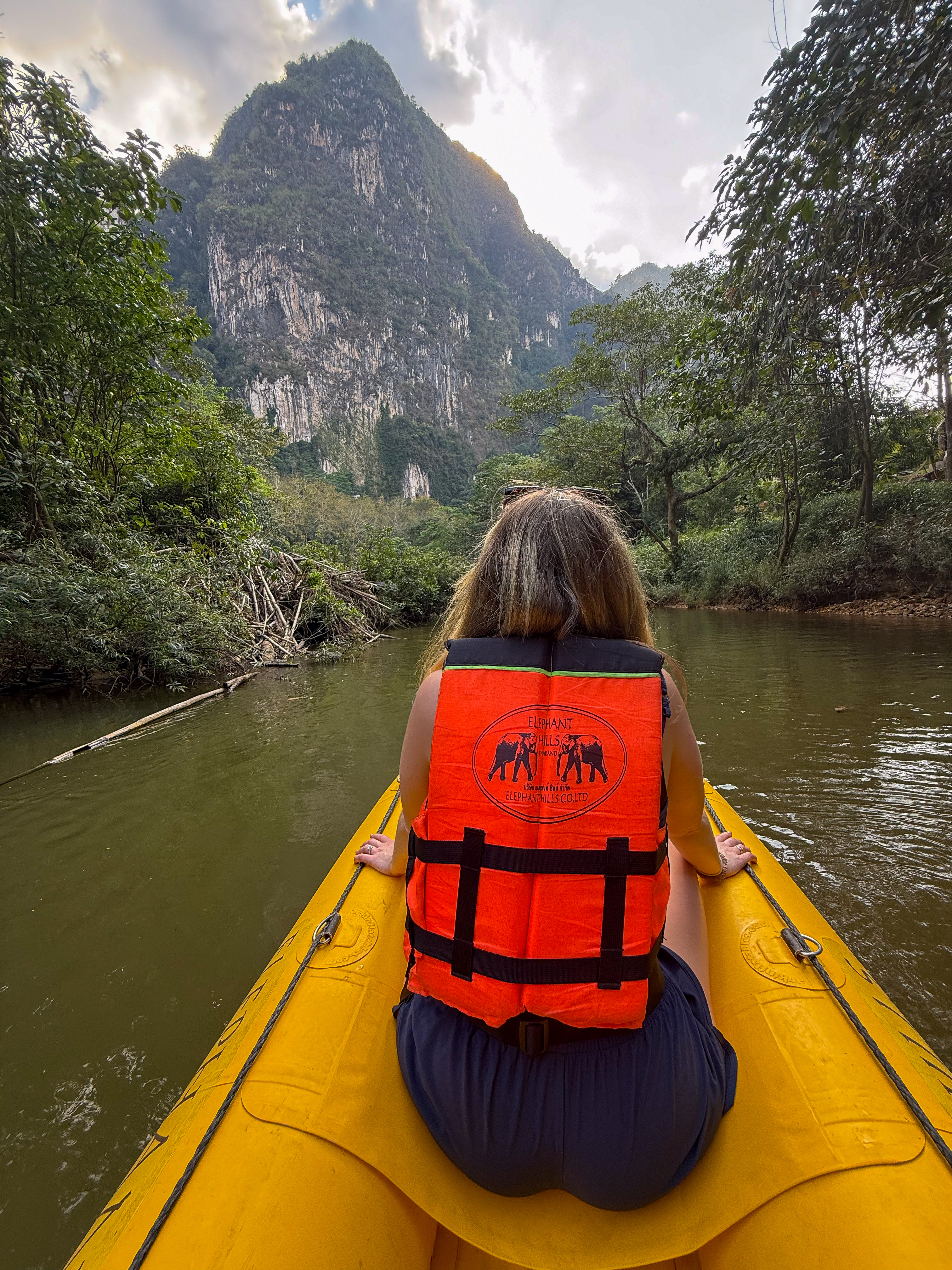 Wearing a bright life vest, a woman enjoys a peaceful canoe ride along the Sok River, framed by dense rainforest and dramatic limestone cliffs.
