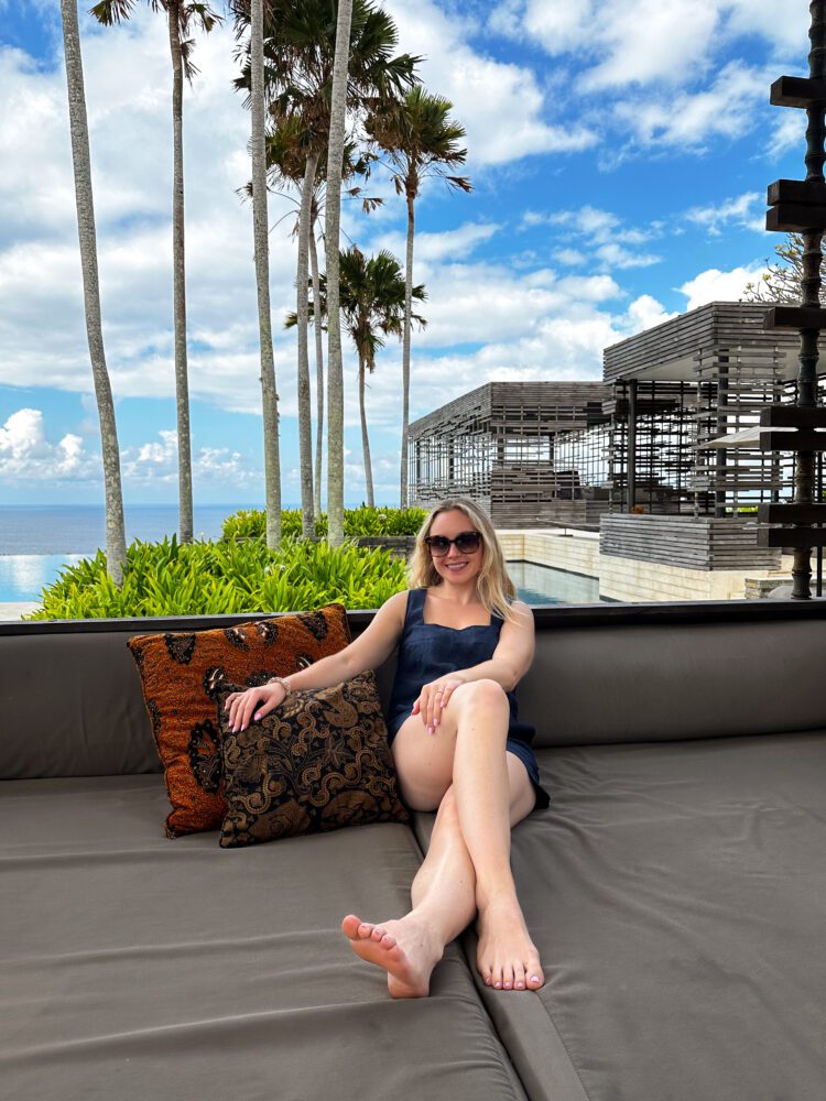 Relaxed woman enjoying a sun-soaked day on an outdoor daybed at Alila Villas Uluwatu, with modern architecture and ocean views in the background.