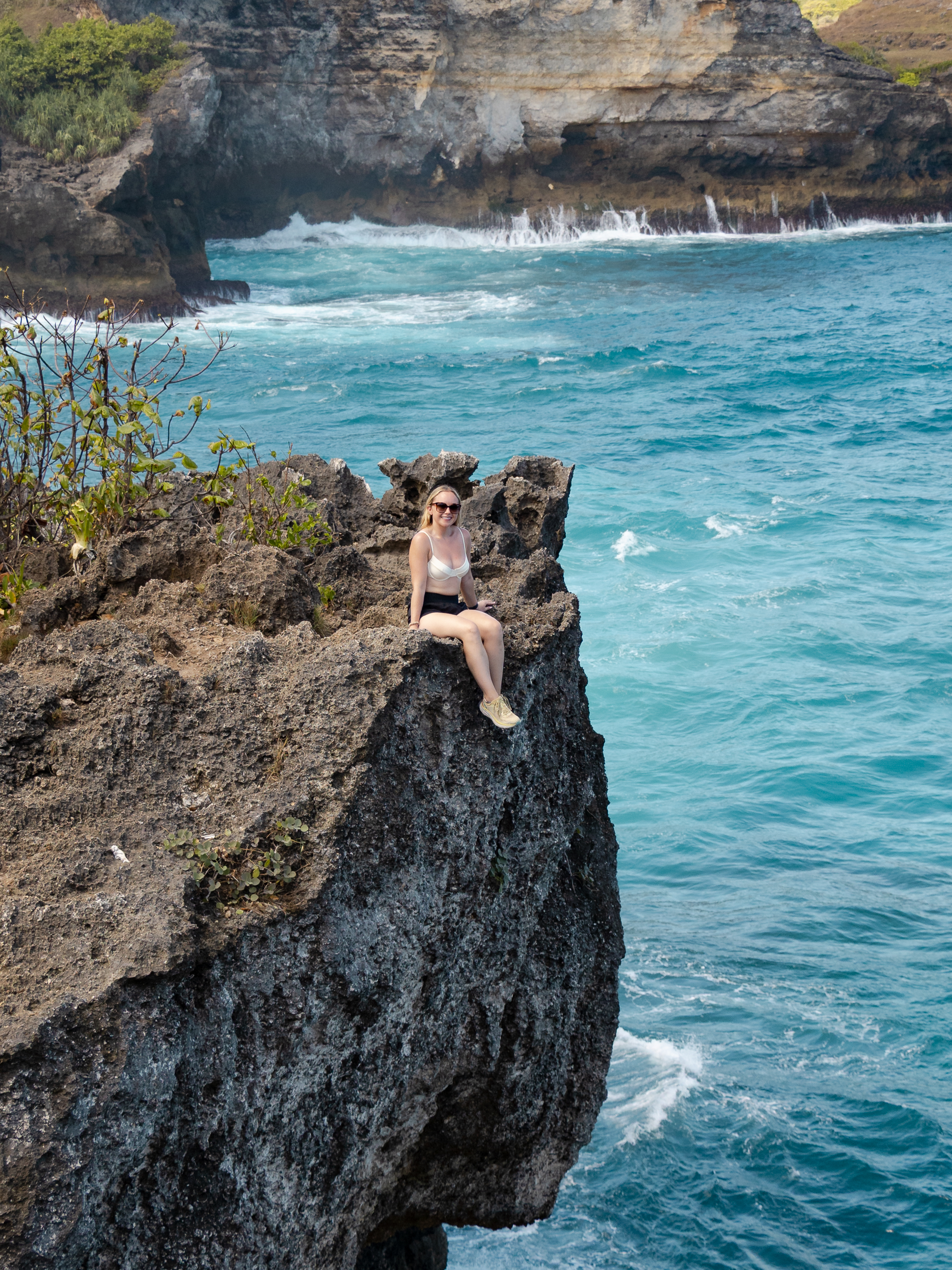 Woman sitting confidently on a rocky cliff edge above turquoise waters at Broken Beach, Nusa Penida.