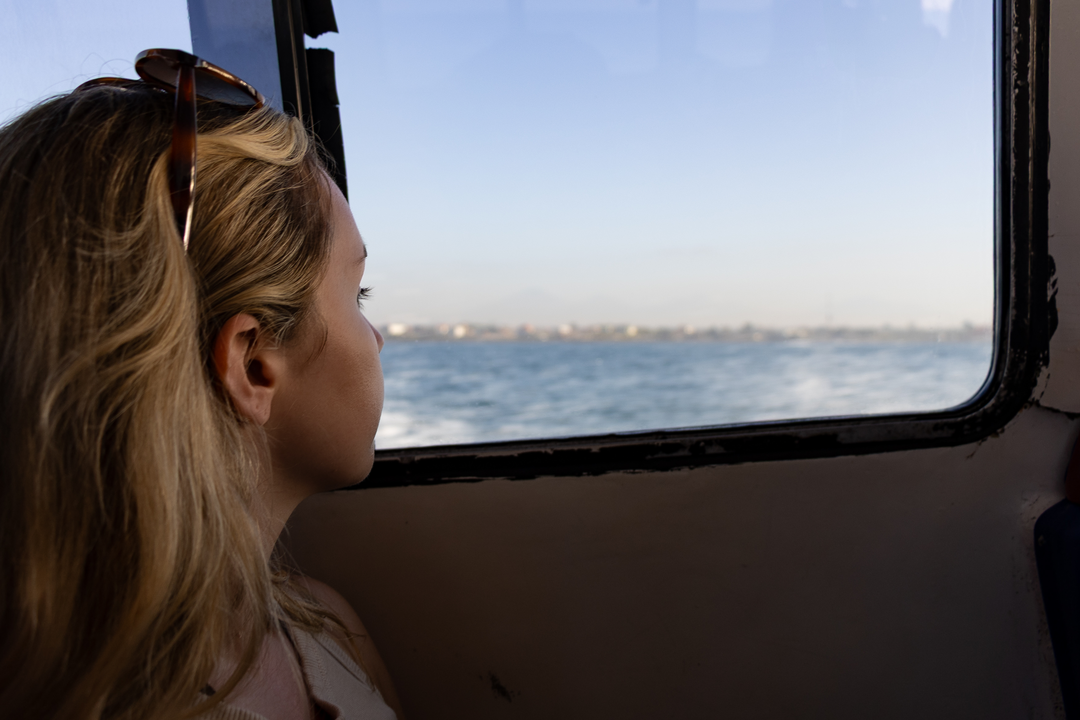 Woman gazing out the window of a fast boat from Sanur to Nusa Penida, with the ocean and distant Bali coastline in view.
