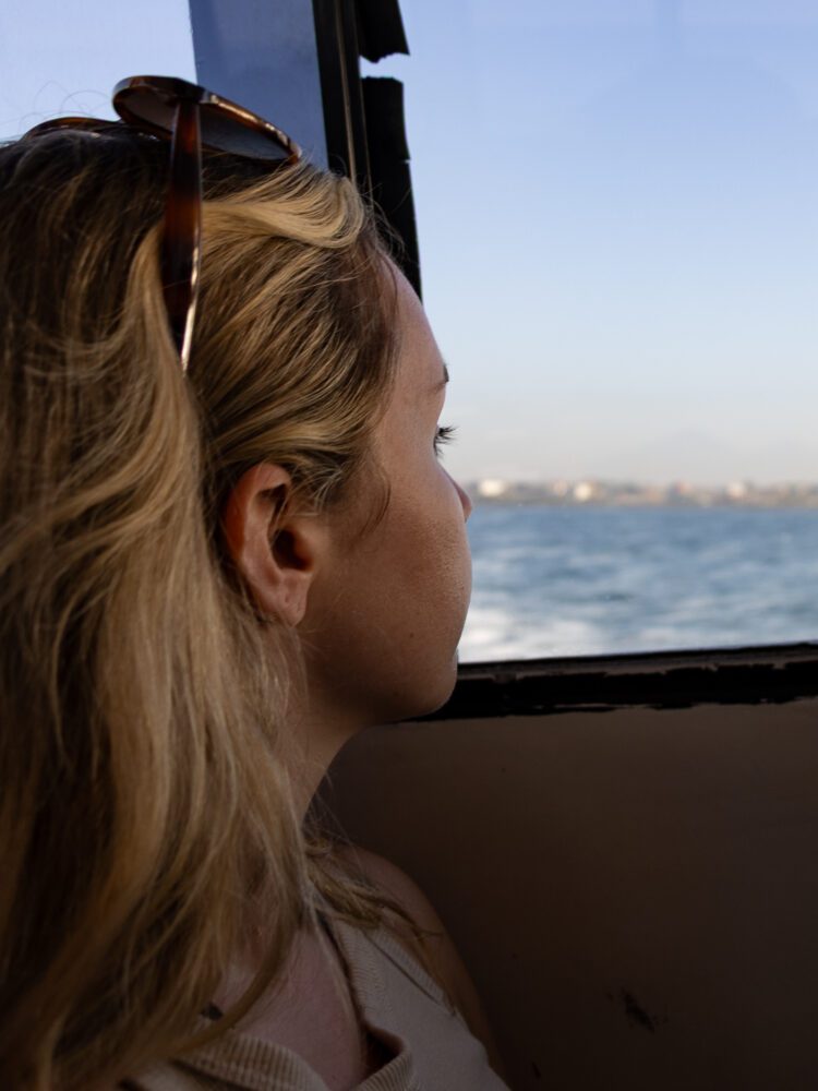 Woman gazing out the window of a fast boat with the ocean and distant coastline visible beyond.