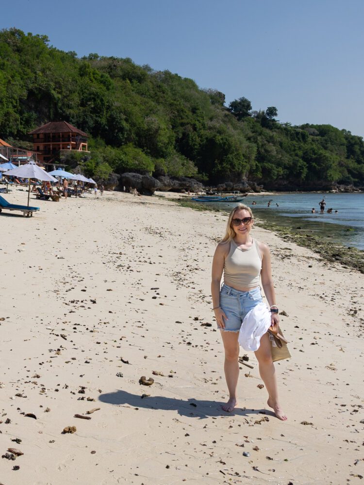 Woman strolling barefoot along the soft sand of Padang Padang Beach, surrounded by lush green cliffs.