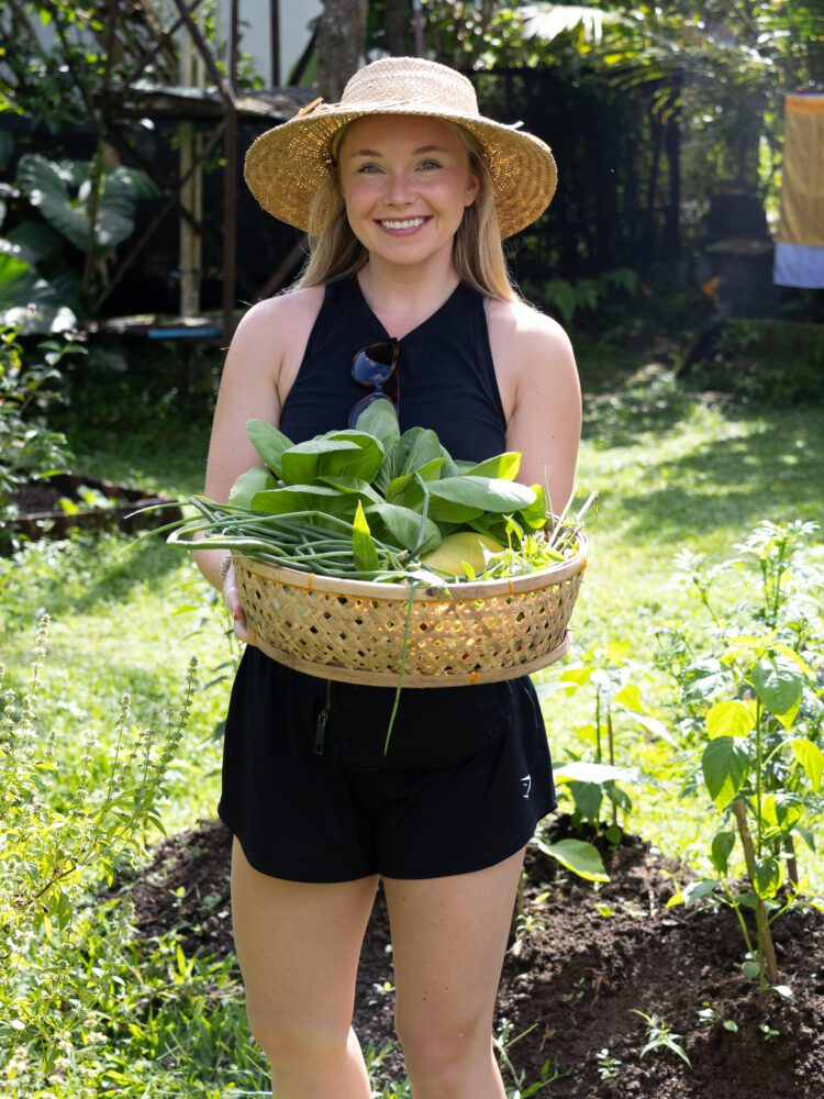 Woman smiling while holding a basket of freshly picked vegetables during a farm-to-table cooking class in Bali.