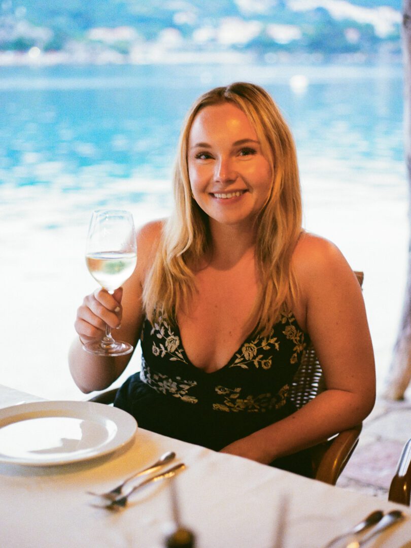 Woman smiling with a glass of white wine at a waterfront table at Gverović-Orsan restaurant near Dubrovnik.