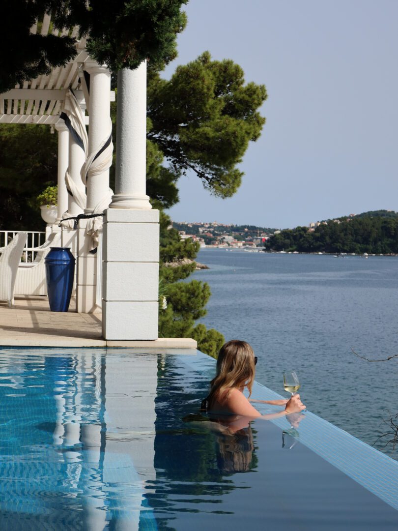 Woman relaxing in an infinity pool with a glass of wine, overlooking the Adriatic Sea at a luxury villa near Dubrovnik.
