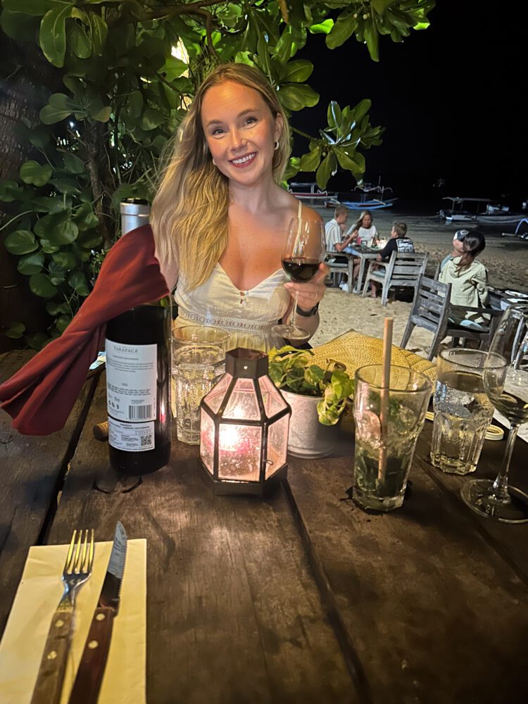 Woman enjoying a romantic beachfront dinner with wine under lantern light at Lilla Pantai in Sanur, Bali.