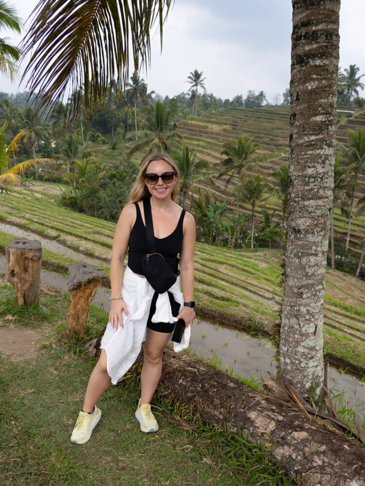 Woman posing in front of the iconic stepped rice terraces of Jatiluwih with lush palms in the background.