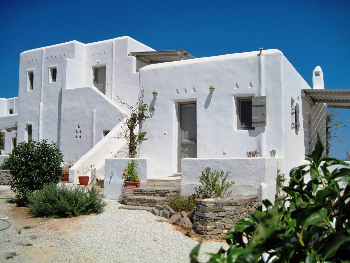 Traditional Cycladic architecture of Aeraki Villas Paros with whitewashed walls, stone paths, and lush greenery.