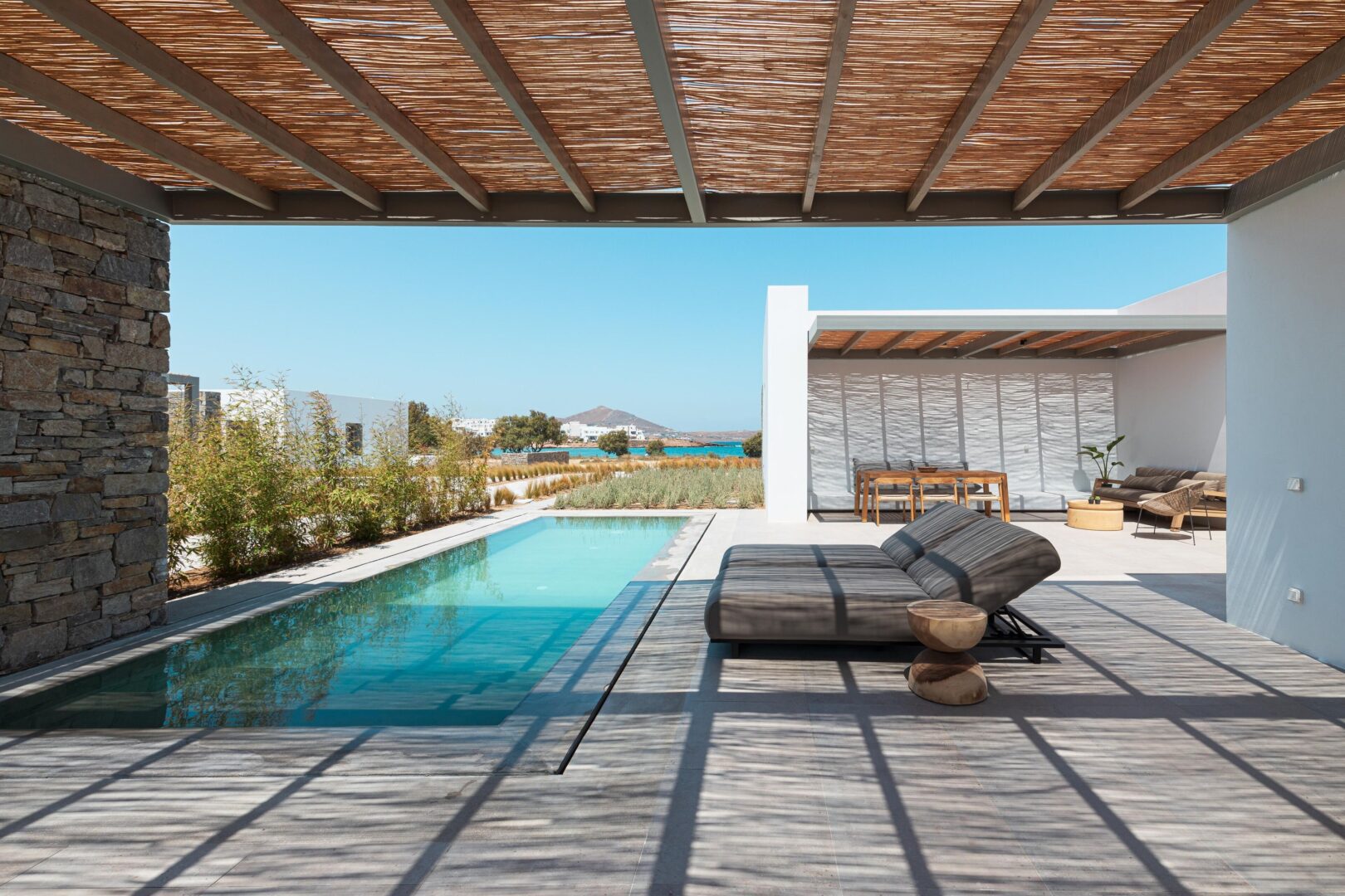 Private terrace with sleek sunbeds, a tranquil plunge pool, and sea views beyond native landscaping.