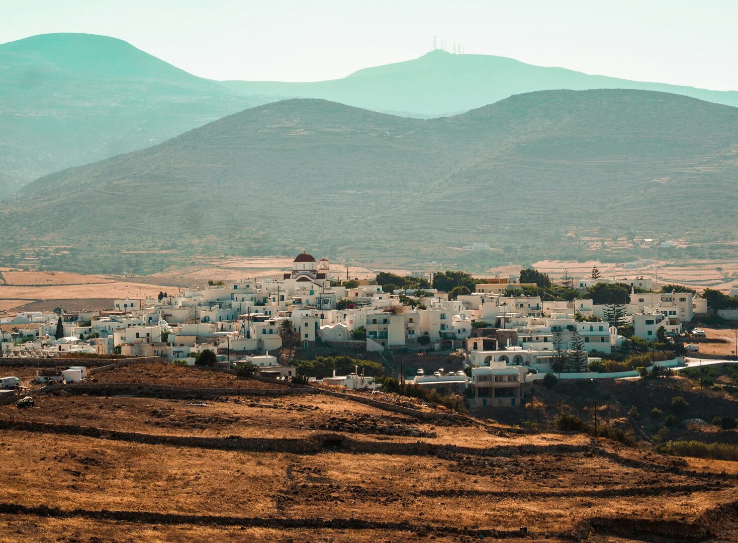 Picturesque hilltop village of Marpissa Paros with white buildings, a red-domed church, and surrounding mountains.