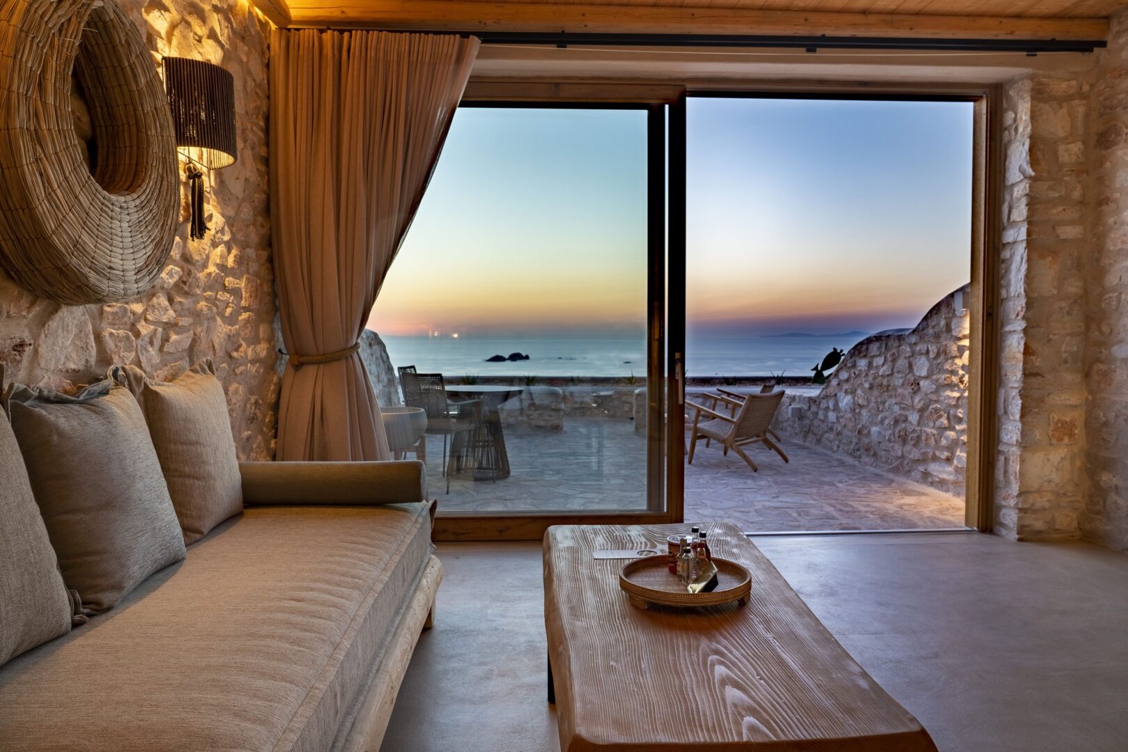 Cozy stone-walled suite with rustic decor opening onto a terrace with sunset views over the Aegean Sea.