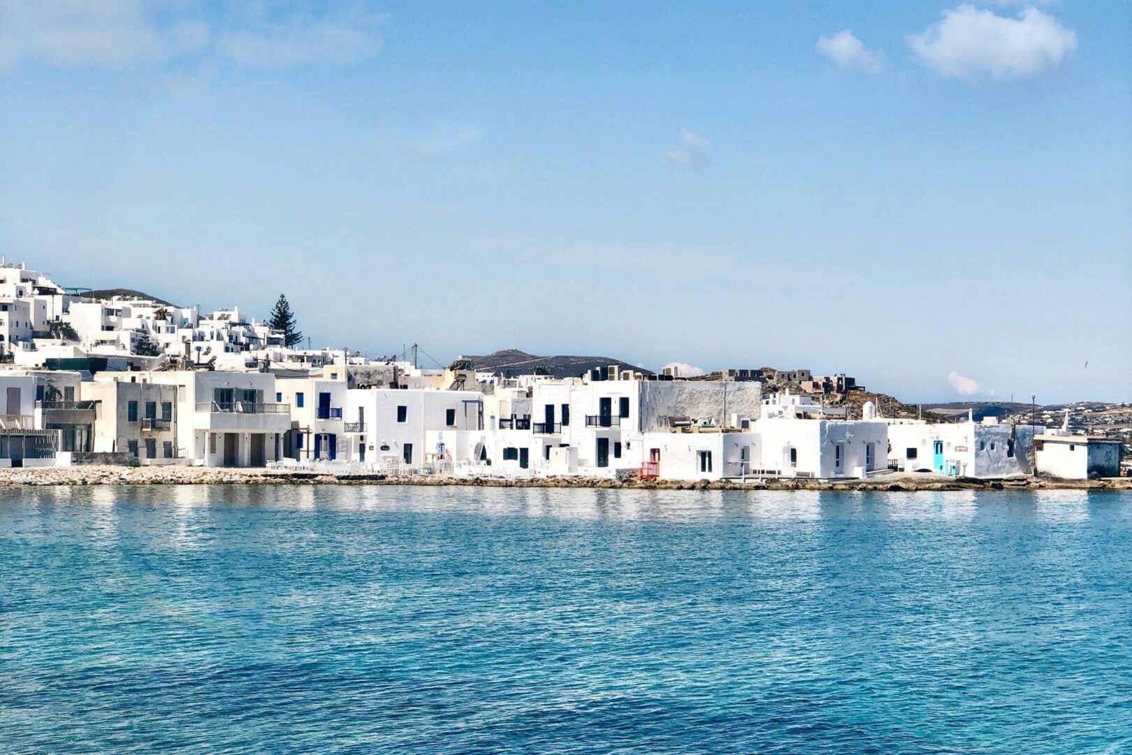 Traditional fishing village of Naoussa Paros with whitewashed buildings lining the waterfront under a clear blue sky.