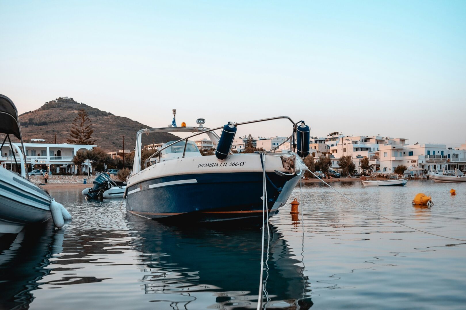 Boats moored in the harbor at Parikia Paros with traditional Cycladic buildings and hills in the background.