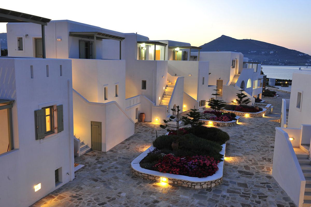 Evening view of Saint Andrea Seaside Resort Paros with illuminated Cycladic buildings, gardens, and pathways near the sea.