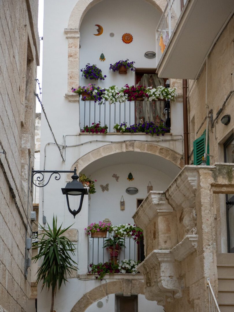 Charming alley in Monopoli, Italy featuring flower-filled balconies and decorative arches in the old town.