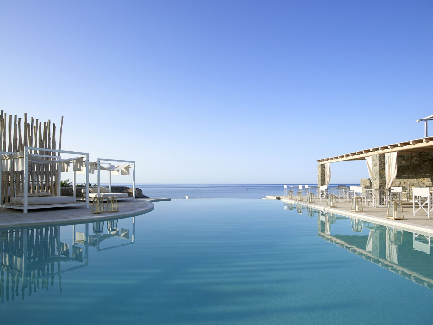 Stylish beachfront pool at Artemis Seaside Resort Milos, with canopy daybeds and a seaside bar overlooking the Aegean.