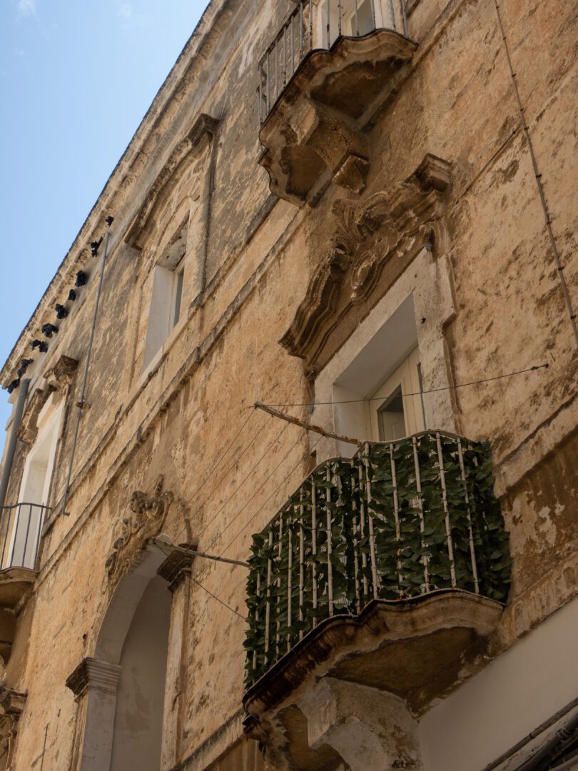Worn stone facade with ornate balconies in Monopoli’s historic old town, showcasing classic Puglian architecture.