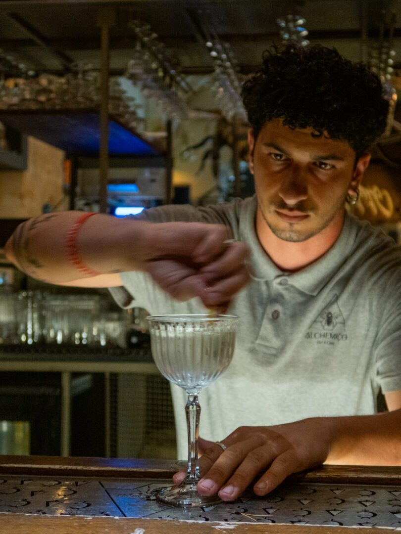 Bartender carefully crafting a cocktail at Alchemico Bar e Cose, a popular nightlife spot in Monopoli, Italy.