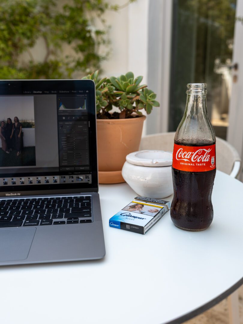 Relaxed photo editing setup with a Coca-Cola, MacBook, and potted plants on a terrace in Puglia, Italy.