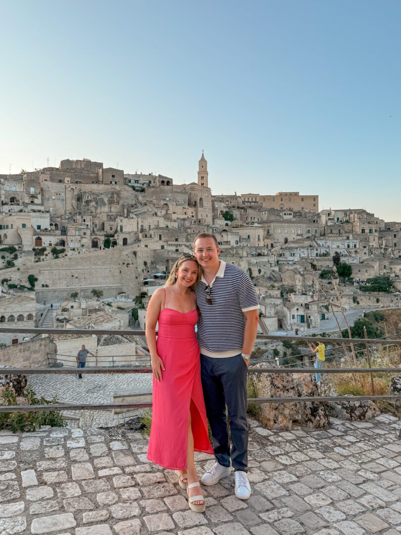 Couple posing at sunset with sweeping views of Matera’s ancient stone buildings and bell tower in the historic old town area.