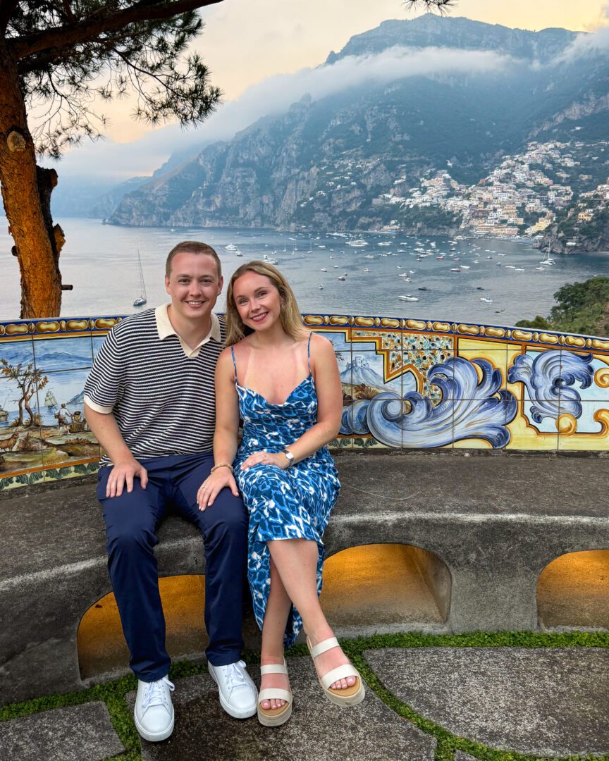 Couple seated on a tiled stone bench at Il San Pietro di Positano’s terrace bar, with dramatic coastal views and pastel evening skies over the Amalfi Coast.